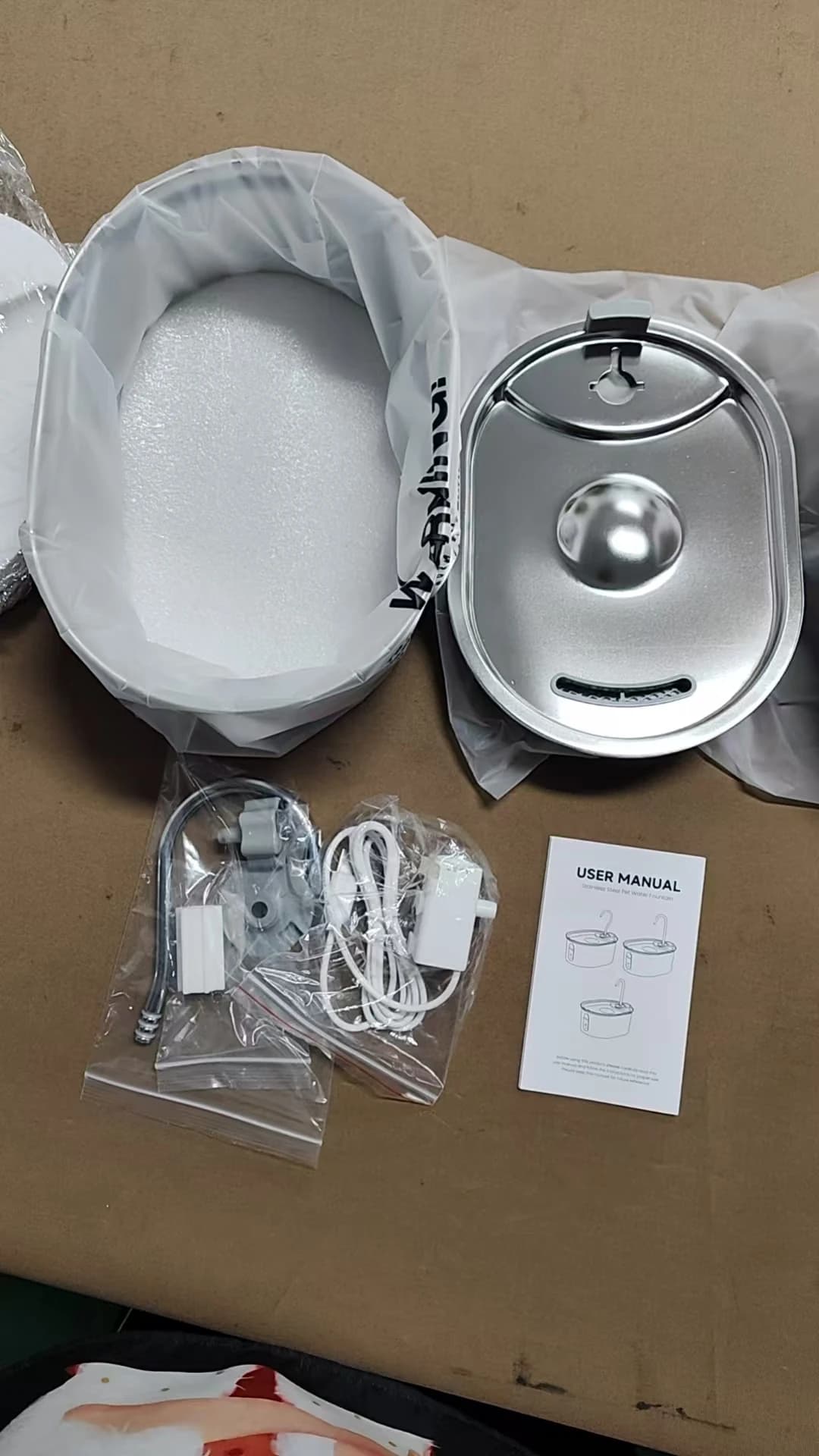 Separate stainless fountain reservoir, drinking tray and packaged pump accessories laid out together