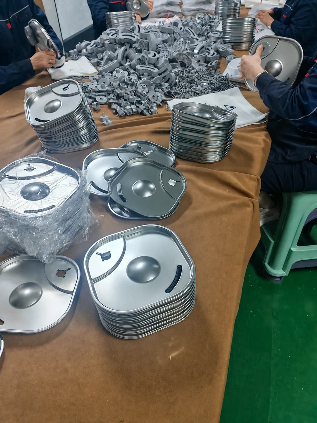 Workers fitting stainless steel trays and gray outlet components at a production table