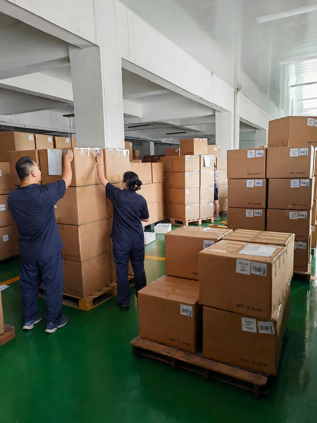 Two workers in matching navy workwear handling palletized outer cartons