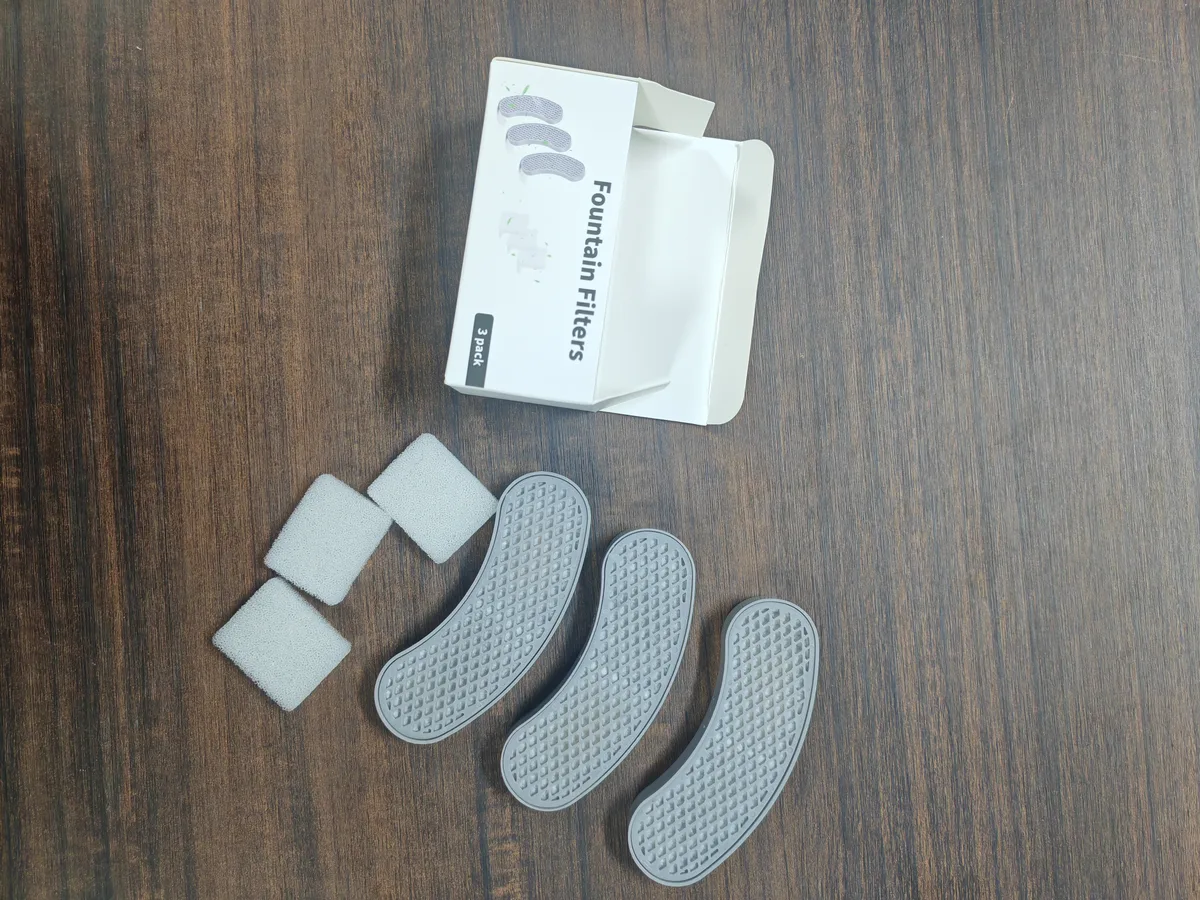 Crescent fountain cartridges and separate foam pre-filter pieces beside an open filter box
